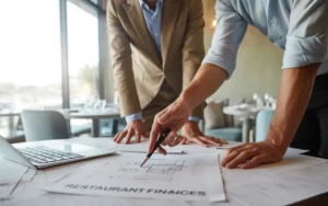 Expert comptable restauration collaborant avec un restaurateur sur des documents financiers et plans de restaurant, autour d'une table de travail moderne, lumière naturelle, ambiance professionnelle et chaleureuse.